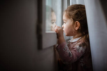 Side view of young girl looking outside window at rain - CAVF66839