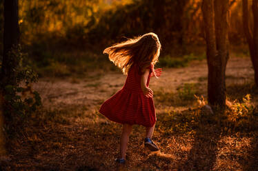 Mädchen läuft durch Bäume mit Licht hinter ihr - CAVF66846