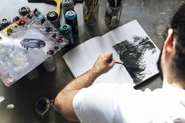 Junger Maler arbeitet an einem Buch auf dem grauen Boden Malerei von vielen Farbe - CAVF66885
