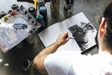 Young painter works on a book on the grey floor painting of many color - CAVF66885