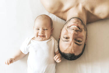 Father and newborn son stretched out in bed laughing - CAVF66903