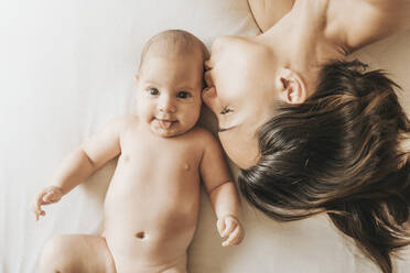 Mutter und neugeborener Sohn im Bett ausgestreckt, Mutter küsst ihren Sohn.das neugeborene Kind streckt die Zunge heraus - CAVF66904