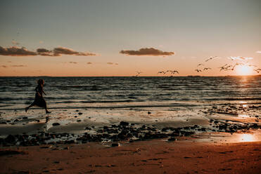 Woman running on the beach in a dress with birds flying - CAVF67008