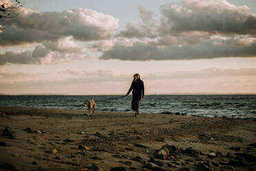 Frau führt Hund in der Abenddämmerung am Strand aus - CAVF67020