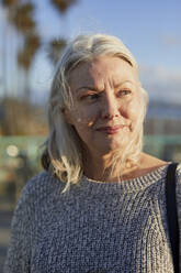 Nahaufnahme einer nachdenklichen älteren Frau, die bei Sonnenuntergang am Strand steht und wegschaut - CAVF67125