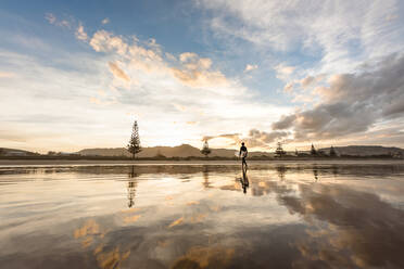 Teen boy with surfboard walking on a beach at sunset - CAVF67135