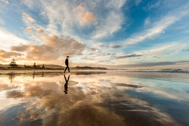 Teenager mit Surfbrett an einem Strand in Neuseeland bei Sonnenuntergang - CAVF67137