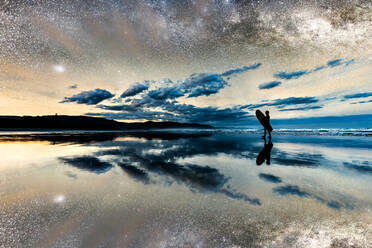 Silhouette Junge hält Surfbrett zu Fuß am Strand unter Sternenhimmel mit Reflexion - CAVF67139