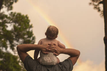 Rückansicht Vater, der seinen Sohn auf den Schultern trägt, während er den Regenbogen betrachtet - CAVF67189