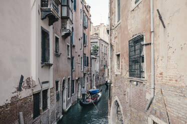 High angle view of man standing in gondola on canal amidst residential buildings in city - CAVF67232