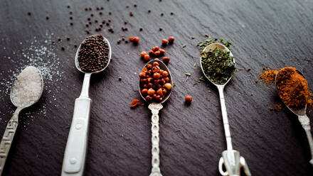 A selection of spices on vintage spoons on a slate chopping board - CAVF67349