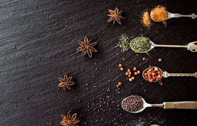 A selection of spices on vintage spoons on a slate chopping board - CAVF67350