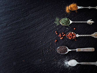 A selection of spices on vintage spoons on a slate chopping board - CAVF67352