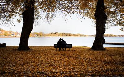 Paar sitzt auf einer Bank umgeben von Herbstlaub und genießt die Landschaft - CAVF67354