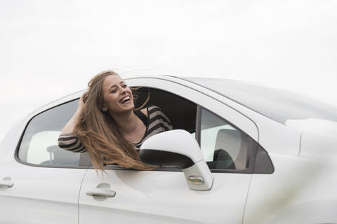 Fröhliche Frau blickt aus dem Autofenster gegen den klaren Himmel, lizenzfreies Stockfoto