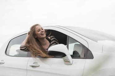 Fröhliche Frau blickt aus dem Autofenster gegen den klaren Himmel - CAVF67417