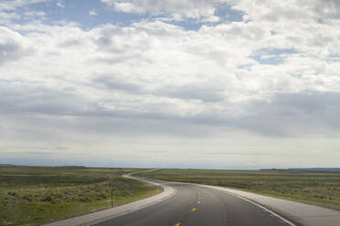 Country road amidst field against cloudy sky at Yellowstone National Park - CAVF67432