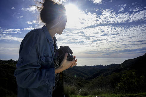 Seitenansicht einer Frau, die eine Kamera hält und gegen den Himmel steht - CAVF67448
