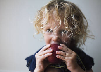 Portrait of girl eating apple against wall at home - CAVF67456