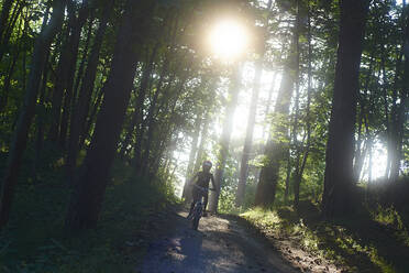 Girl riding bicycle on dirt road in forest - CAVF67462