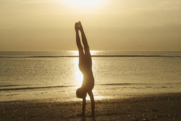 Full length of silhouette girl doing handstand at beach against sky during sunset - CAVF67463