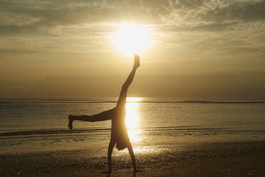 Silhouette Mädchen macht Handstand am Strand gegen den Himmel bei Sonnenuntergang - CAVF67465
