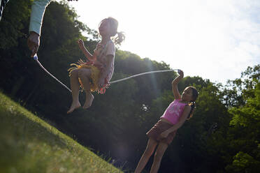 Mother and daughters playing with jump rope at park during summer - CAVF67466