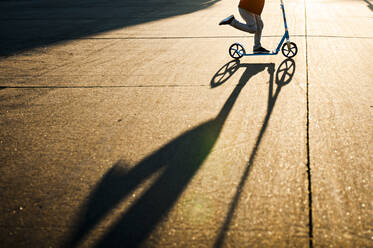 Untere Hälfte eines Jungen, der im Sonnenlicht mit einem Schatten auf der Straße schnell rollt - CAVF67630