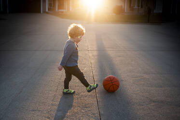 Kleinkind Junge kicking Basketball im Freien auf der Straße in ziemlich Licht - CAVF67631