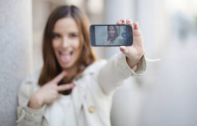 Woman taking selfie while leaning by wall - CAVF67658