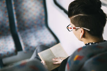 High angle view of woman reading book in train - CAVF67661