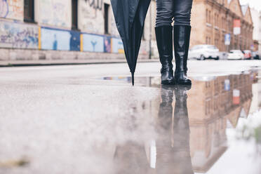 Tiefschnitt einer Frau mit Regenschirm auf einer Straße in der Stadt - CAVF67669
