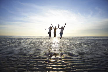 Weibliche Freunde springen am Strand gegen den Himmel - CAVF67712