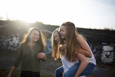 Teenager-Mädchen schaut sich Freunde an, die an einem sonnigen Tag Huckepack nehmen - CAVF67720