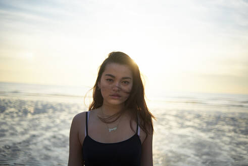 Portrait of confident teenage girl standing at beach during sunset - CAVF67724