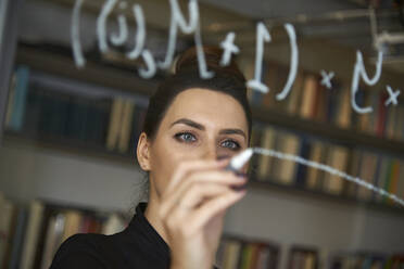 Geschäftsfrau schreibt Formel auf Glaswand im Büro - CAVF67727
