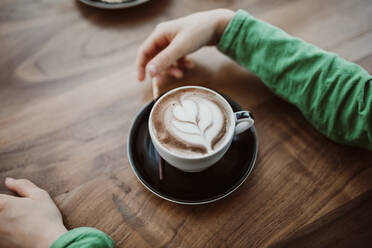 Abgeschnittene Hände eines Jungen mit Kaffee am Tisch in einem Cafe - CAVF67737