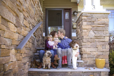 Portrait of sisters with kissing parents and dogs on steps against house - CAVF67759