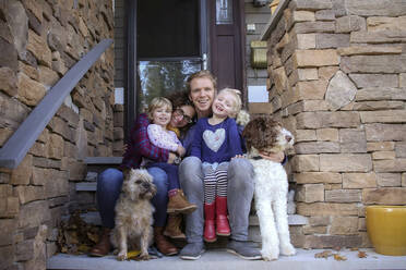 Portrait of happy family with dogs sitting on steps against house - CAVF67760