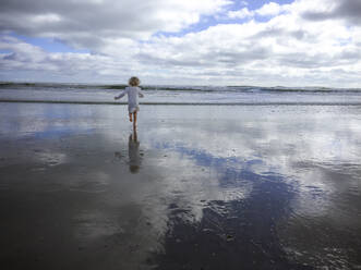 Rückansicht eines Mädchens, das am Strand von St. Augustine gegen den bewölkten Himmel läuft - CAVF67765
