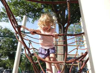 Unbeschwertes Mädchen klettert am Seil auf dem Klettergerüst auf dem Spielplatz - CAVF67771