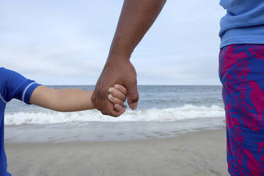 Ausgeschnittenes Bild von Vater und Sohn, die sich am Strand an den Händen halten - CAVF67778