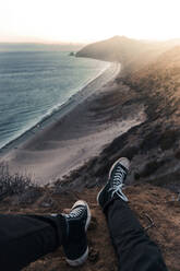 Ausgeschnittenes Bild eines Mannes, der bei Sonnenuntergang auf einem Felsen am Meer sitzt - CAVF67854