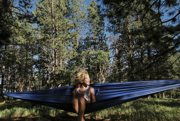 Fröhliches Mädchen, das sich in einer Hängematte an Bäumen im Wald ausruht - CAVF67864