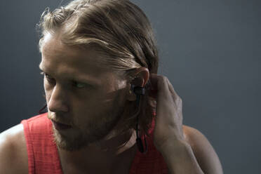 Serious man adjusting hair while listening music in gym against wall - CAVF67937