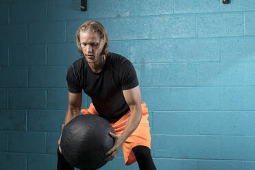 Mann mit Medizinball beim Training gegen die Wand im Fitnessstudio - CAVF67938