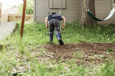Rear view of playful boy swinging at playground - CAVF67994