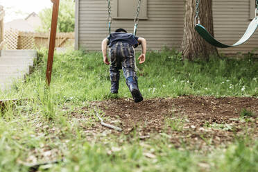 Rückansicht eines verspielten Jungen, der auf einem Spielplatz schaukelt - CAVF67994