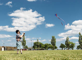 In voller Länge von Jungen fliegen amerikanische Flagge Drachen im Park gegen bewölkten Himmel - CAVF67996