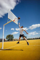 Ein Mann spielt Basketball auf einem gelben Platz und dunkt ein - OCMF00846